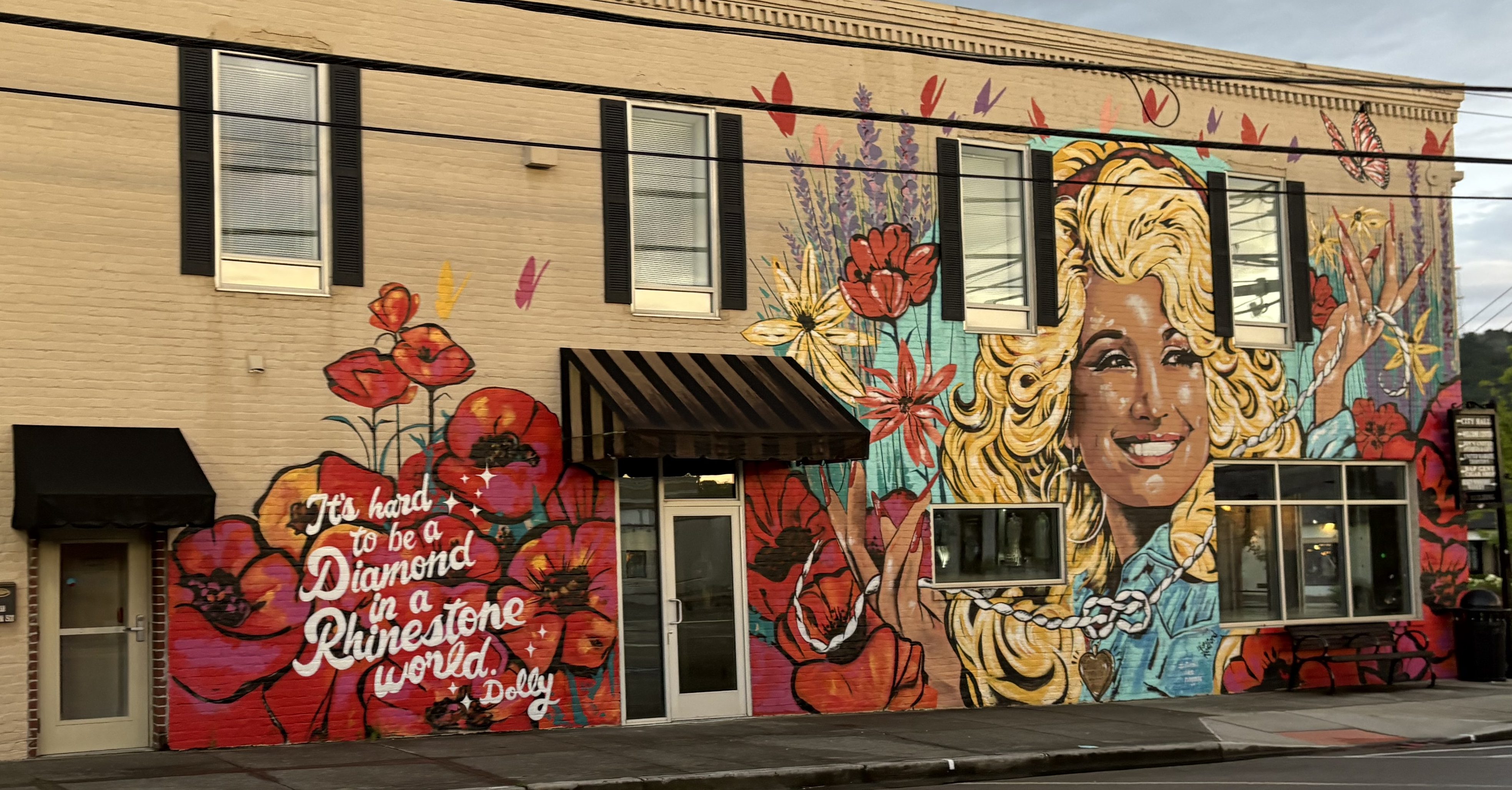Mural celebrating Dolly Parton in Ringgold, Georgia. It is on a tan brick building with a picture of Dolly, red flowers, and the words "It's hard to be a diamond in a rhinestone world".